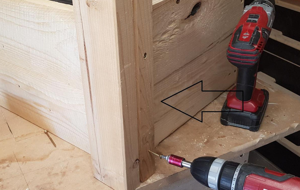 A wooden leg is screwed to the side of a wooden box with an Einhell cordless screwdriver, an arrow points to the spot.