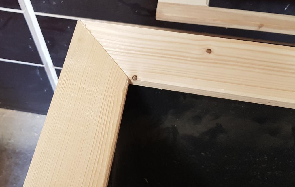 Close-up of a light wooden frame with a miter cut at the corner, on a black surface.