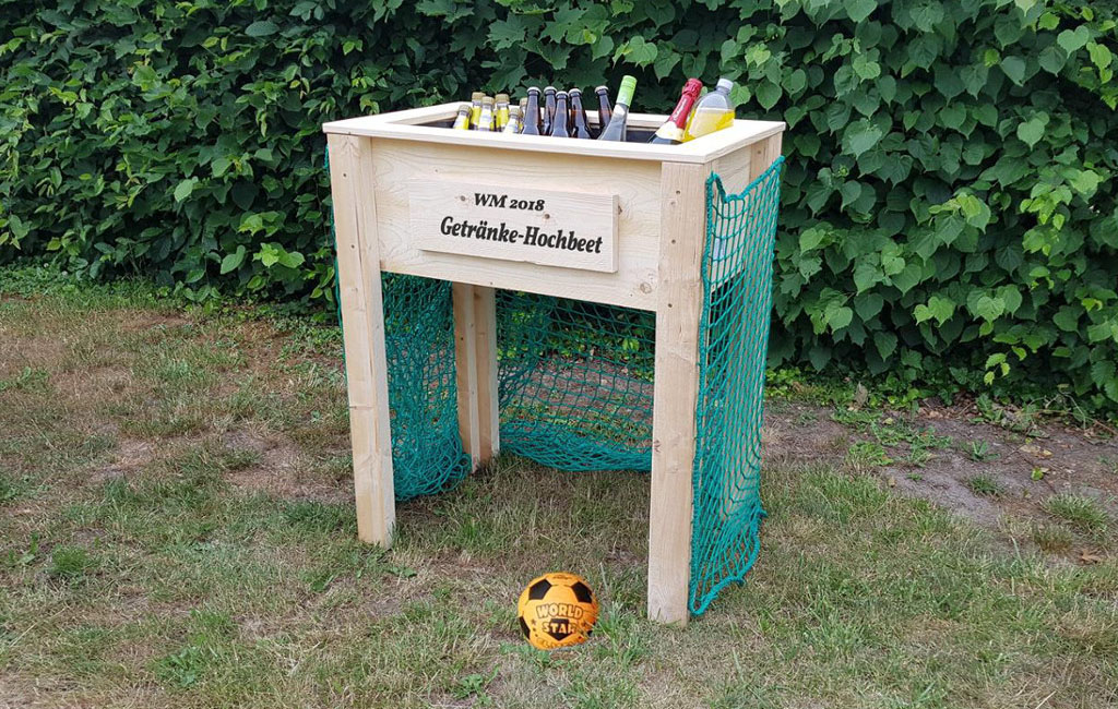 A raised bed with bottles used as a drink bar, green nets on the sides. Text on the bed: "WM 2018 Getränke-Hochbeet".