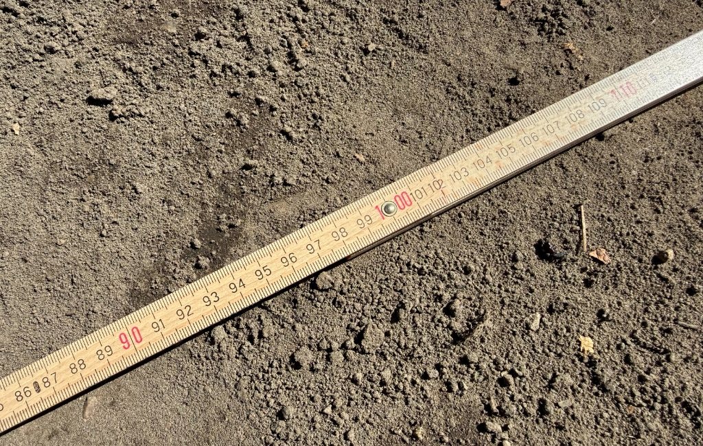 Nahaufnahme eines Gliedermaßstabs auf dunkler Erde, der einen Bereich von etwa 100 Zentimetern anzeigt.