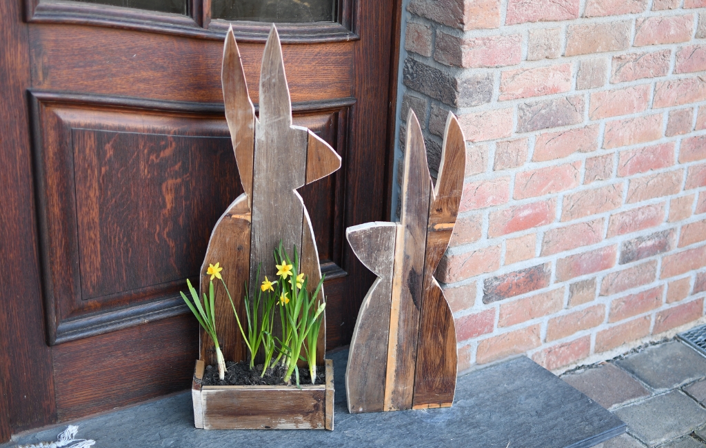 Zwei Holzhasen und eine Kiste mit gelben Blumen stehen vor einer Haustür.