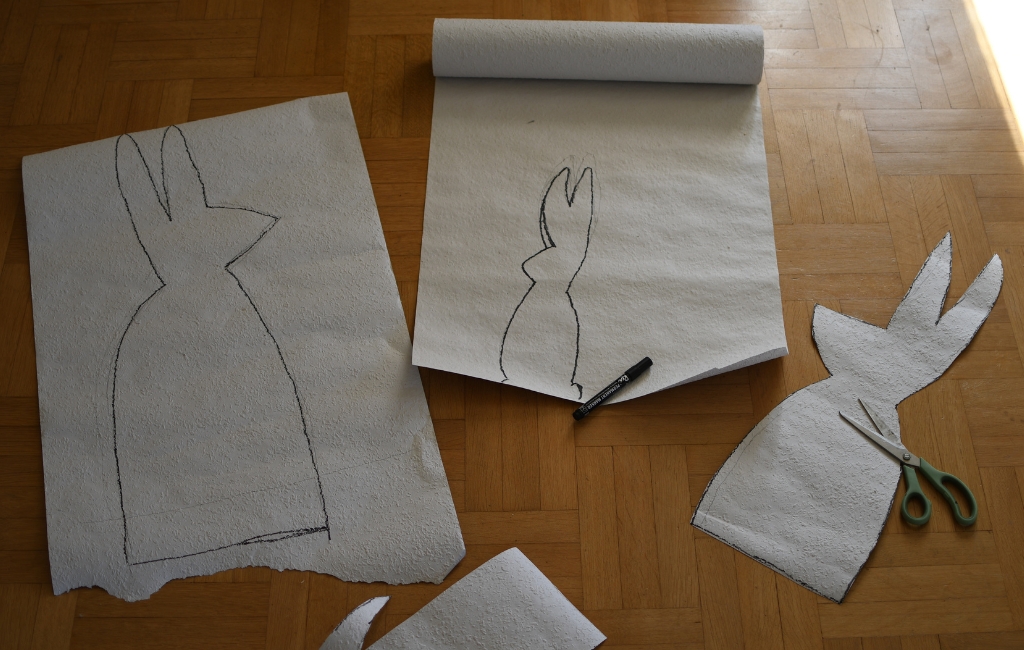 Auf Papier gezeichnete Hasenform wird mit Schere ausgeschnitten, daneben Stift und weitere Vorlagen.