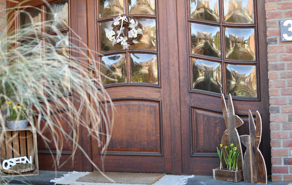 Zwei Holzhasen und eine Kiste mit gelben Blumen stehen vor einer Haustür.