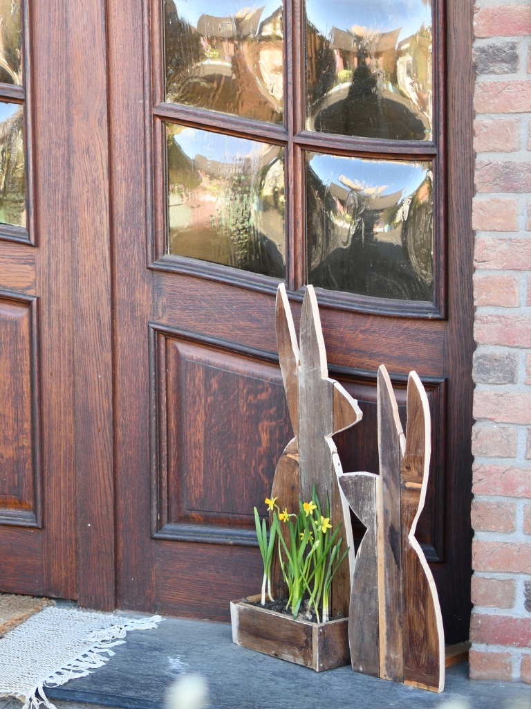 Zwei Holzhasen und eine Kiste mit gelben Blumen stehen vor einer Haustür.