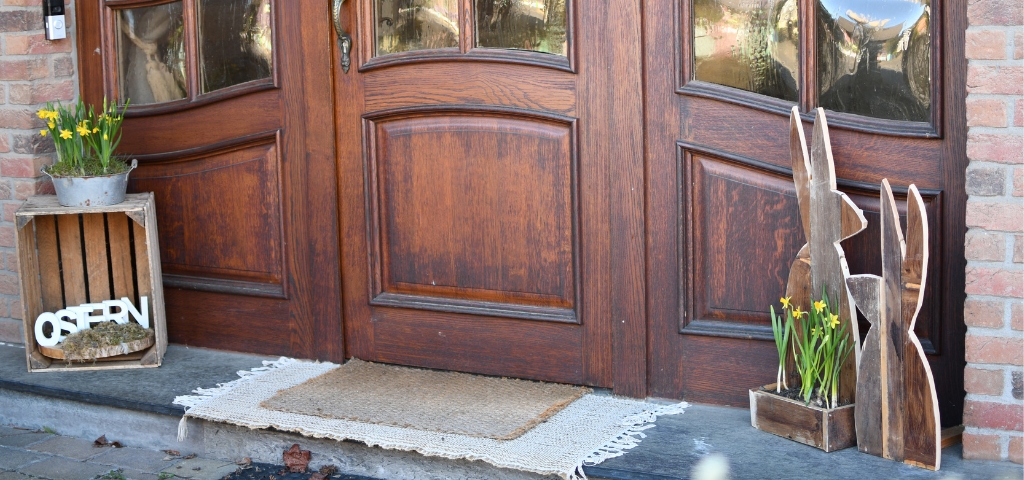 Zwei Holzhasen und eine Kiste mit gelben Blumen stehen vor einer Haustür.