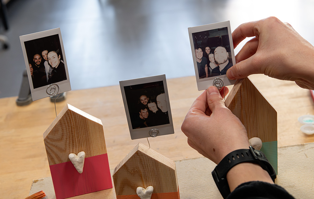 Eine Person steckt ein Sofortbild in den Drahtclip eines fertigen Holzaufstellers.