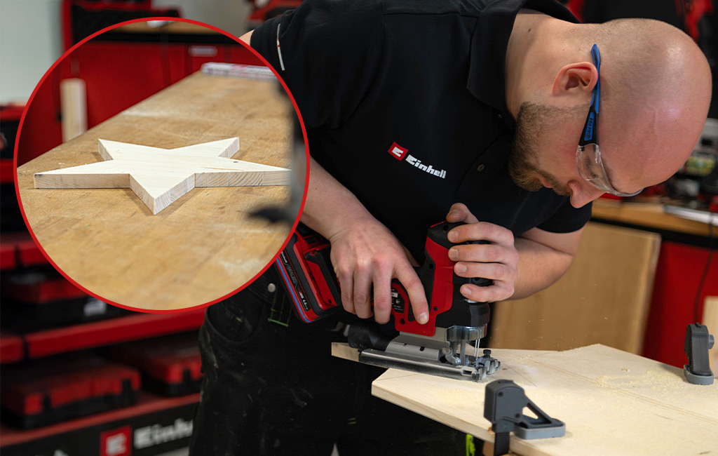 Eine Person sägt mit einer Stichsäge einen Holzstern aus einer Holzplatte aus; ein fertiger Stern ist im Detail gezeigt.