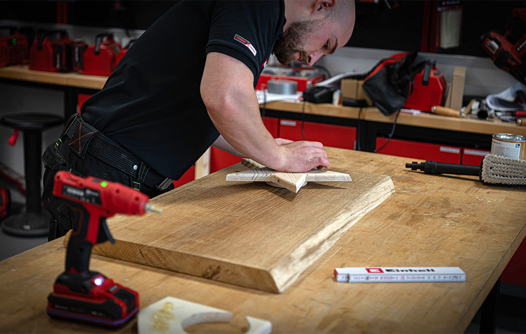 Eine Person bearbeitet ein Holzbrett mit einer sternförmigen Holzfigur darauf in einer Werkstatt.