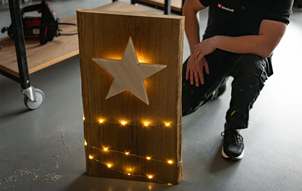 Eine große Holzplatte mit einem eingesetzten Holzstern und umlaufender Lichterkette steht aufrecht auf dem Boden.