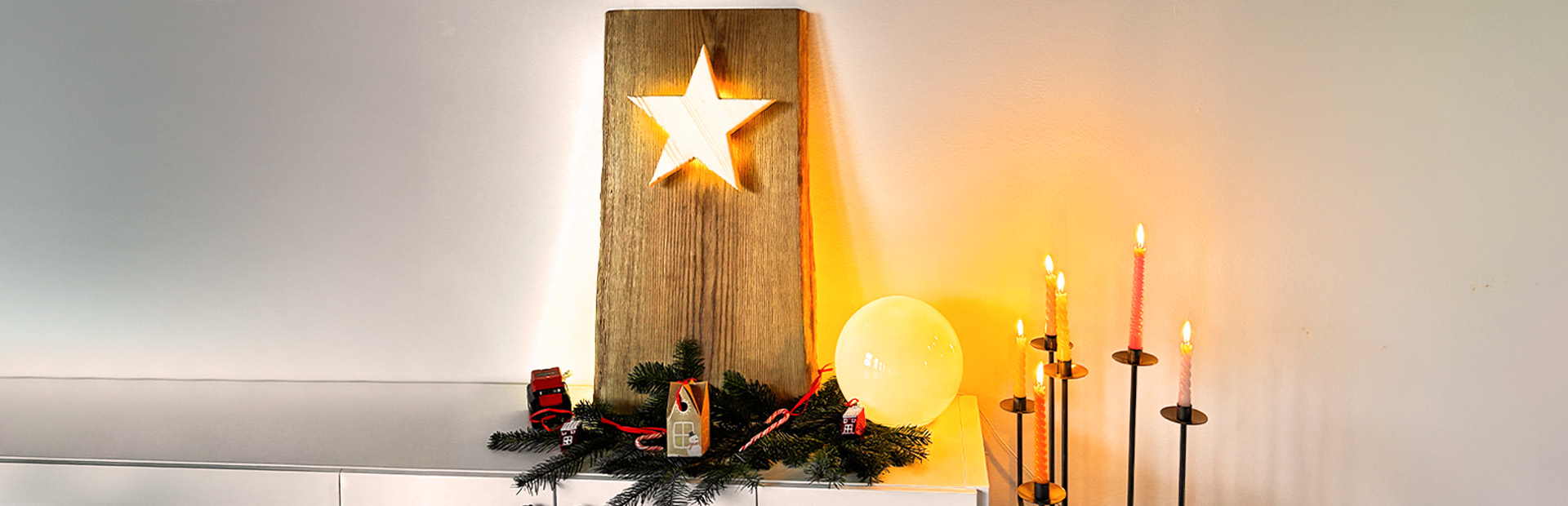 Ein beleuchteter Holzstern ist in eine große Holzplatte eingelassen, dekoriert mit Tannenzweigen und Kerzen.