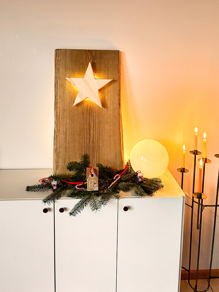 Ein beleuchteter Holzstern ist in eine große Holzplatte eingelassen, dekoriert mit Tannenzweigen und Kerzen.