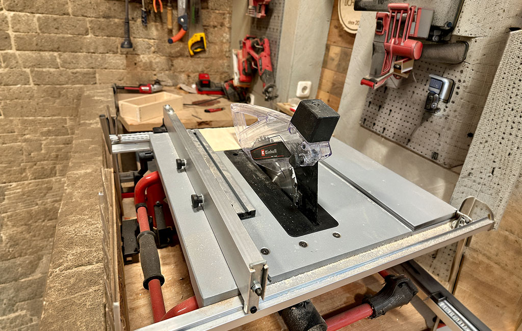 Table saw in a workshop with visible circular saw blade and guard, mounted on a workbench ready for cutting wood.