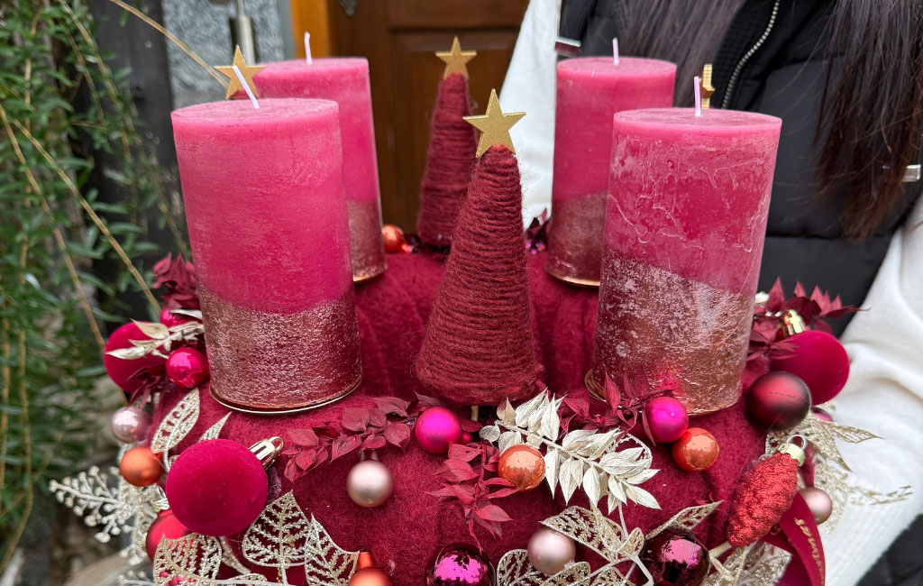 A festively decorated Advent wreath with four red candles, red felt trees, and many baubles.