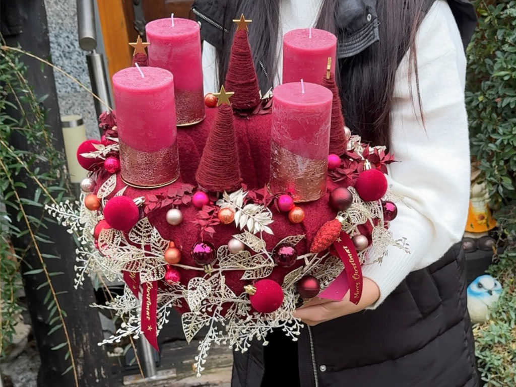 Close-up of the finished Advent wreath with red candles, baubles, golden leaves, and red felt trees.
