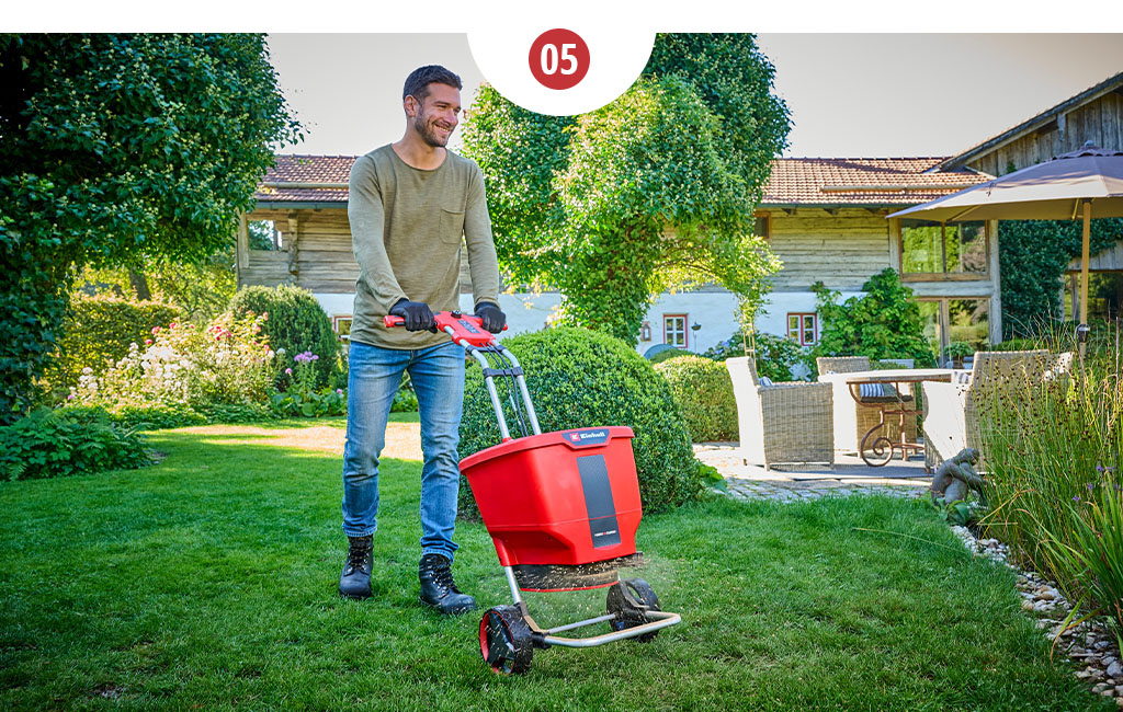 A man fertilising the lawn in the garden with an Einhell cordless spreader.