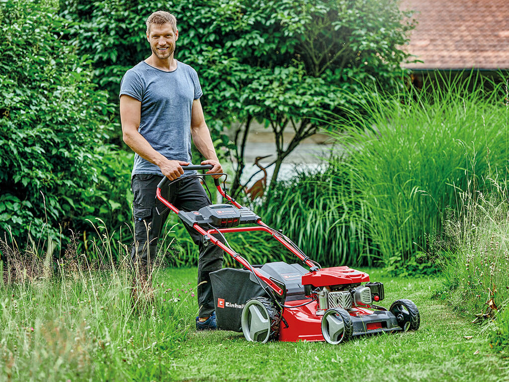 Ein Mann steht hinter einem Einhell Benzin-Rasenmäher mit Akku-Start-Automatik.