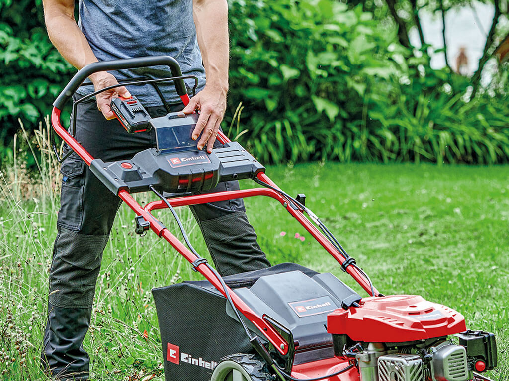 a man puts a battery into the lawnmower