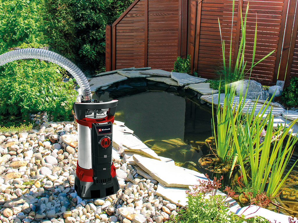 Einhell dirty water pump beside a garden pond with stones, plants and a small waterfall.