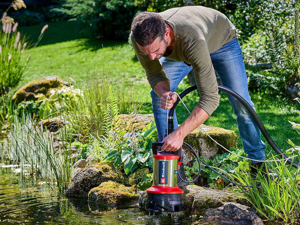 Ein Mann saugt einen Gartenteich mit einer Einhell-Schmutzwasserpumpe ab.