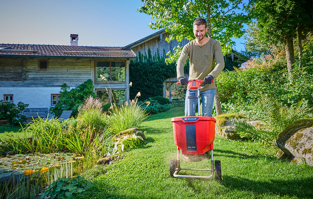 Ein Mann mit einem Einhell Akku-Streuwagen beim Verteilen von Dünger im Garten