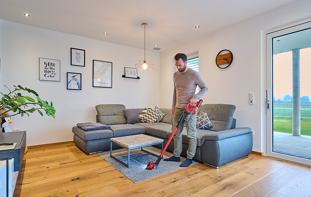 Ein Mann saugt mit einem roten Einhell Nass-Trockensauger einen Teppich im Wohnzimmer.