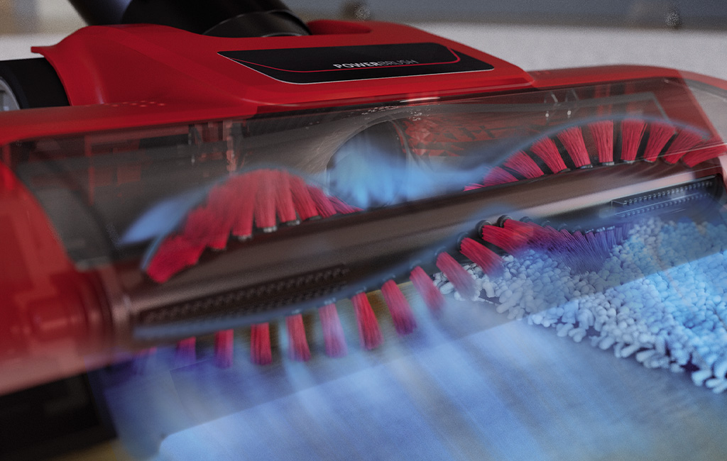 Detailansicht einer rotierenden Bürstenwalze mit roten und schwarzen Borsten auf einem Teppich.