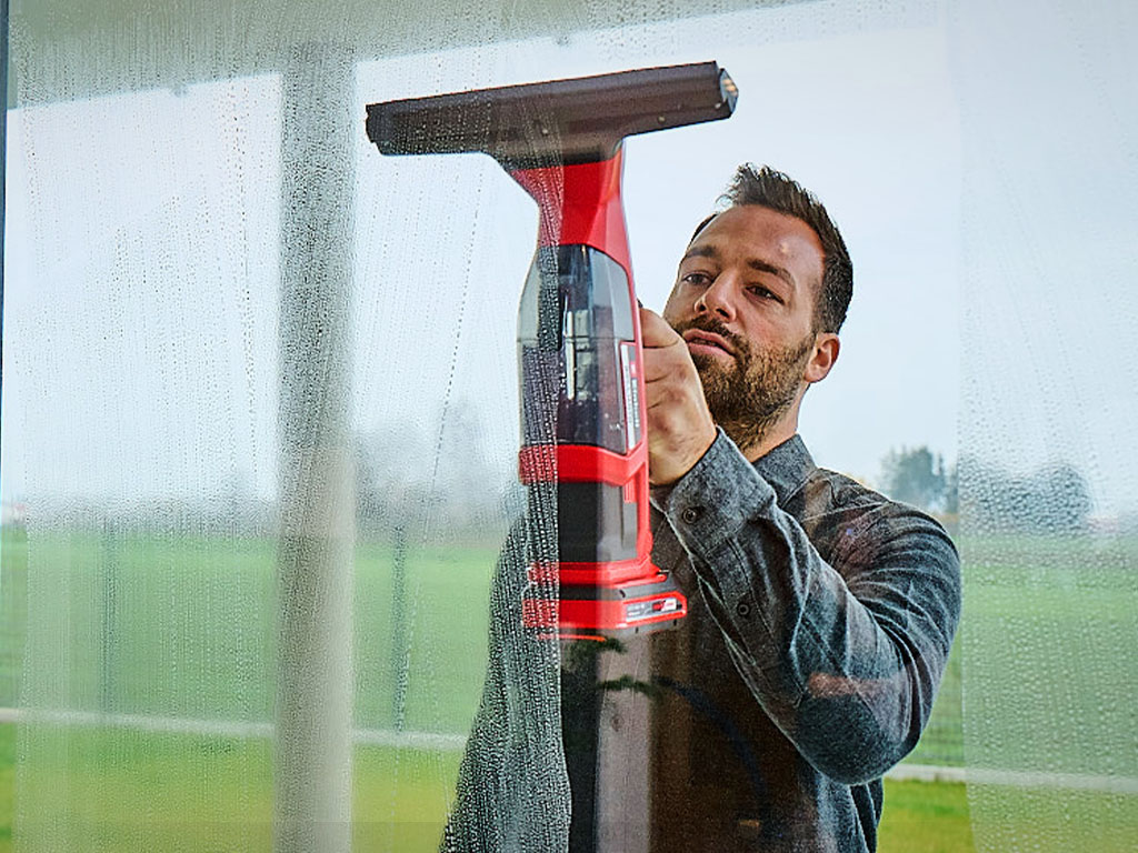 Man cleans window with the Einhell cordless window cleaner BRILLIANTO