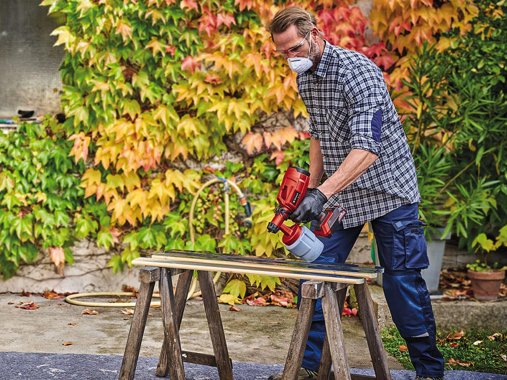 man sprays paint on wooden beams