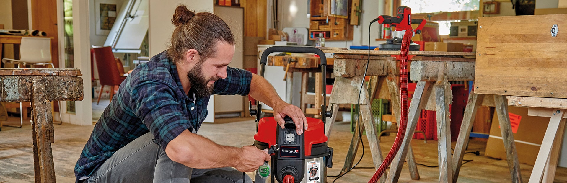 A man uses an Einhell wet and dry vacuum cleaner while working at a workbench.