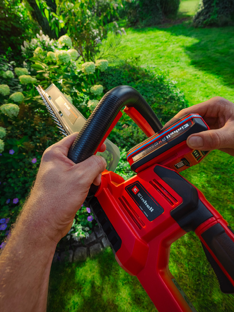 Hand setzt einen Einhell-Akku in eine Heckenschere ein.