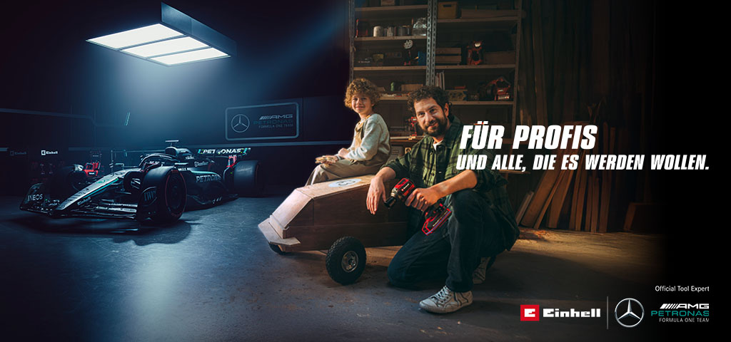 Ein Vater und sein Kind sitzen in einer Werkstatt vor einem selbstgebauten Seifenkistenauto. Im Hintergrund steht ein Mercedes-AMG PETRONAS Formel-1-Wagen mit Einhell-Werkzeugen daneben. Rechts der Text: „Für Profis und alle, die es werden wollen.“