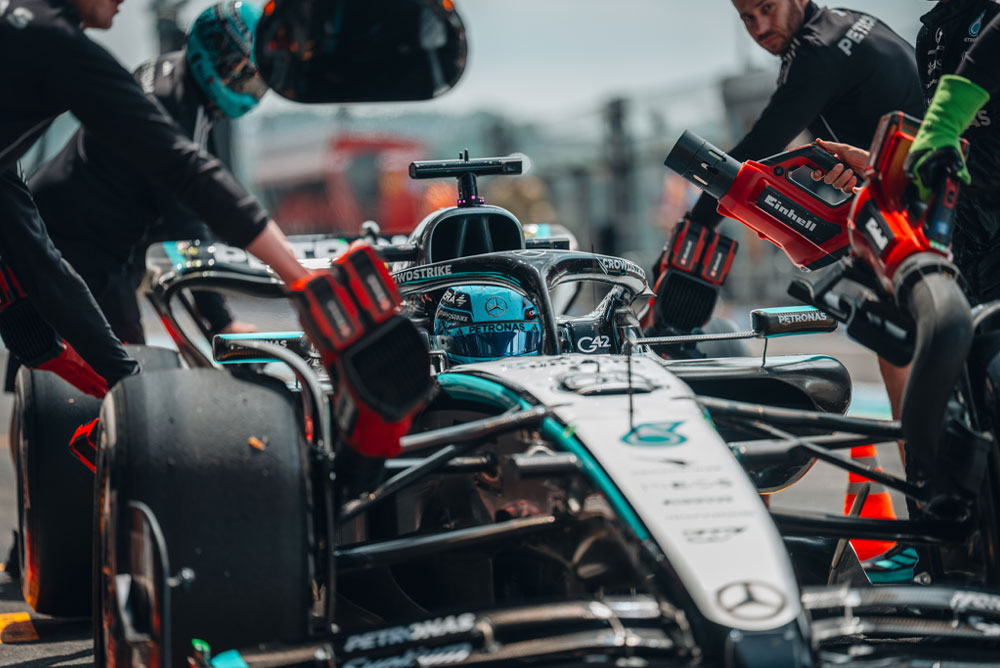 Una vettura di Formula 1 del team Mercedes-AMG PETRONAS durante un pit stop. I membri del team utilizzano soffiatori a batteria Einhell per raffreddare i componenti del veicolo. La squadra lavora con concentrazione e precisione.