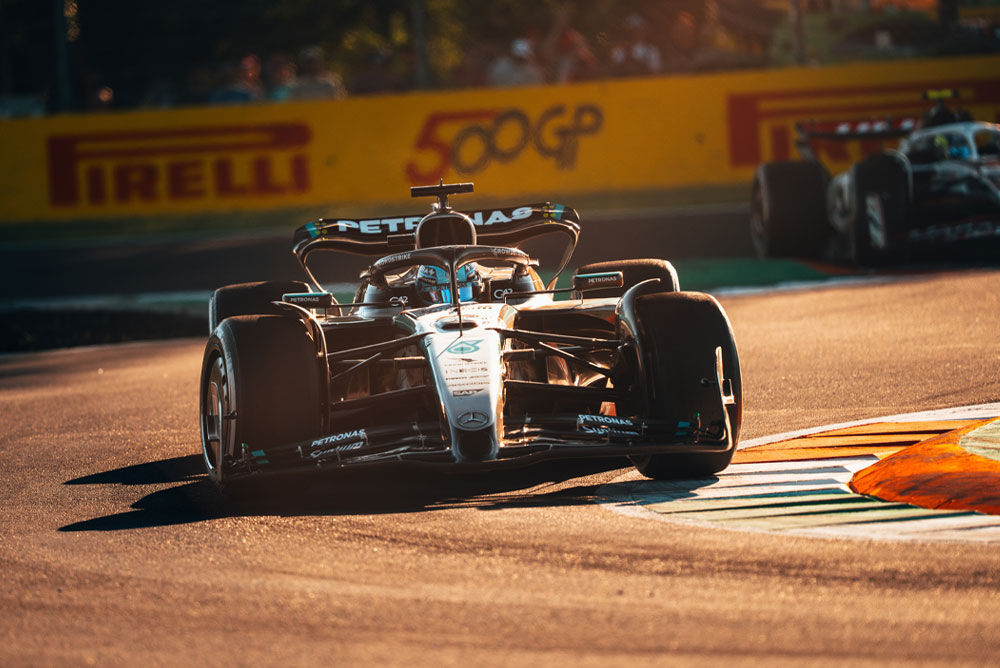 Una vettura di Formula 1 Mercedes-AMG PETRONAS in gara su un circuito illuminato dal sole durante un Gran Premio. L’auto affronta una curva ad alta velocità, con un’altra vettura sullo sfondo.