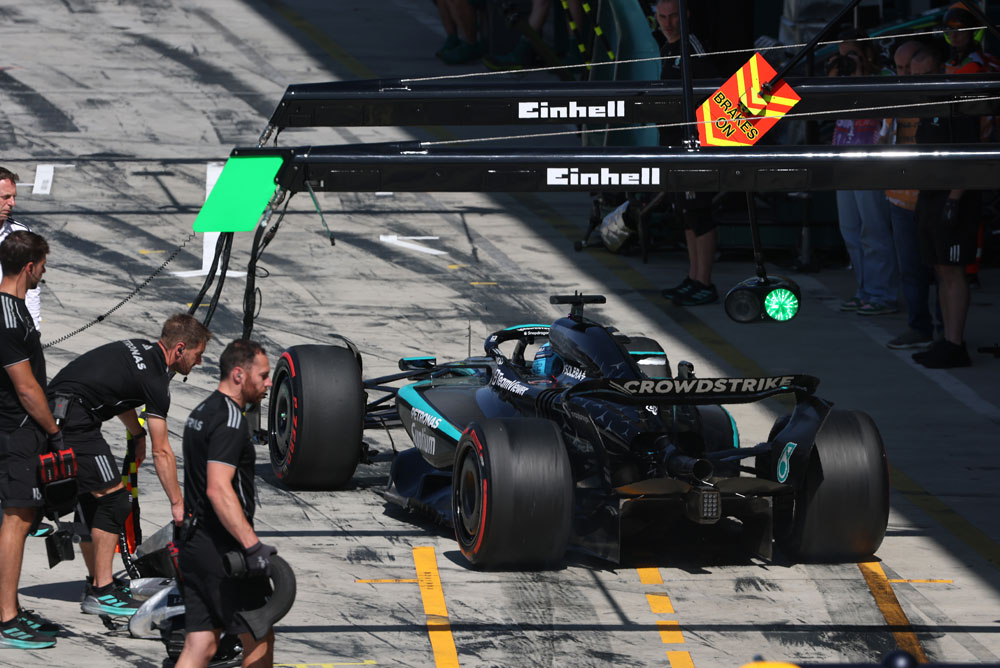 Un'auto di Formula 1 della Mercedes-AMG PETRONAS nella corsia dei box durante un pit stop. Diversi membri del team circondano l'auto. Il marchio Einhell è visibile sopra l'area dei box.