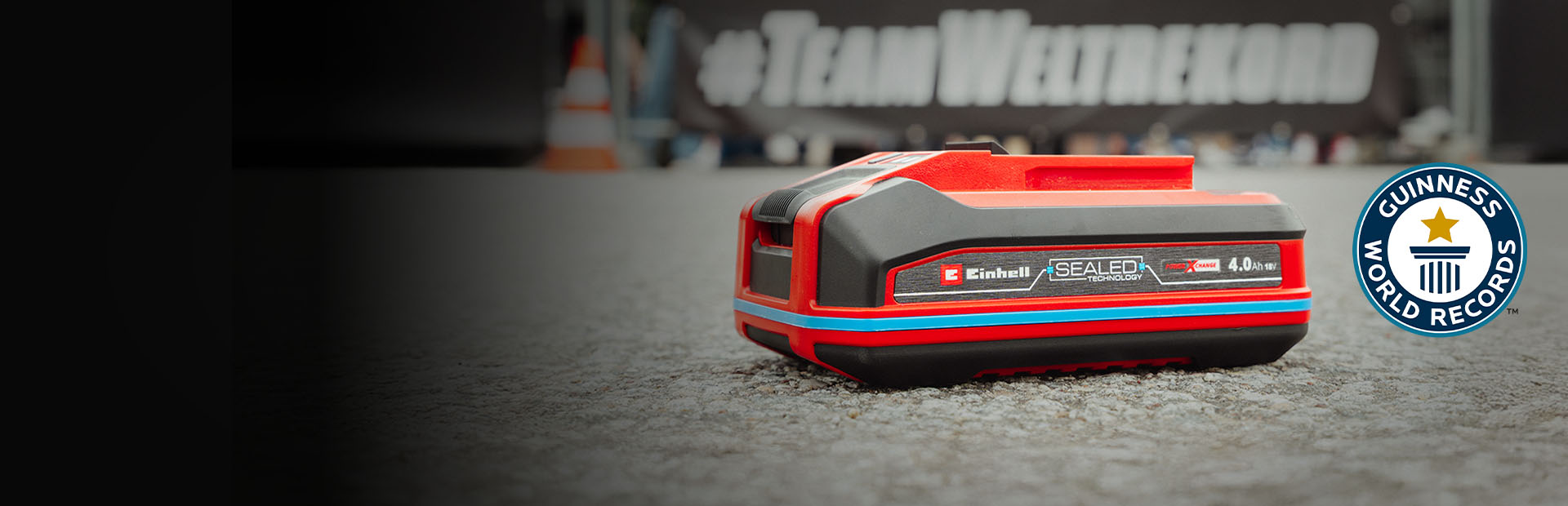 Batteria Einhell SEALED Power X-Change 4.0 Ah posata sull’asfalto, con il logo Guinness World Records «Record Holder» a destra.
