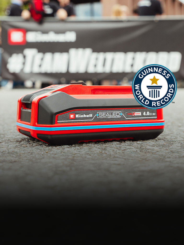Batteria Einhell SEALED Power X-Change 4.0 Ah posata sull’asfalto, con il logo Guinness World Records «Record Holder» a destra.