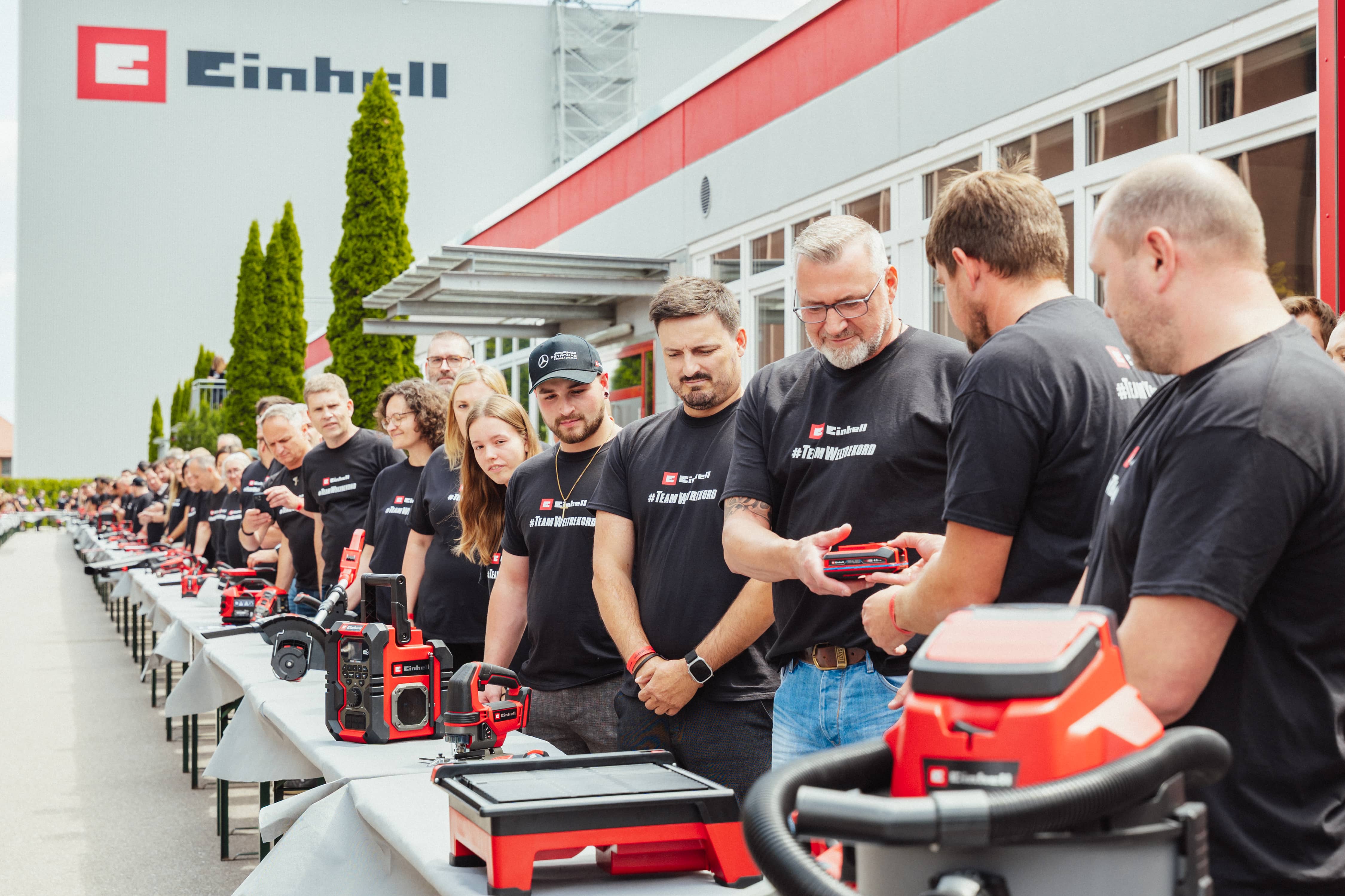 Einhell-Mitarbeitende stehen an Tischen mit Geräten und reichen sich einen SEALED Akku weiter.