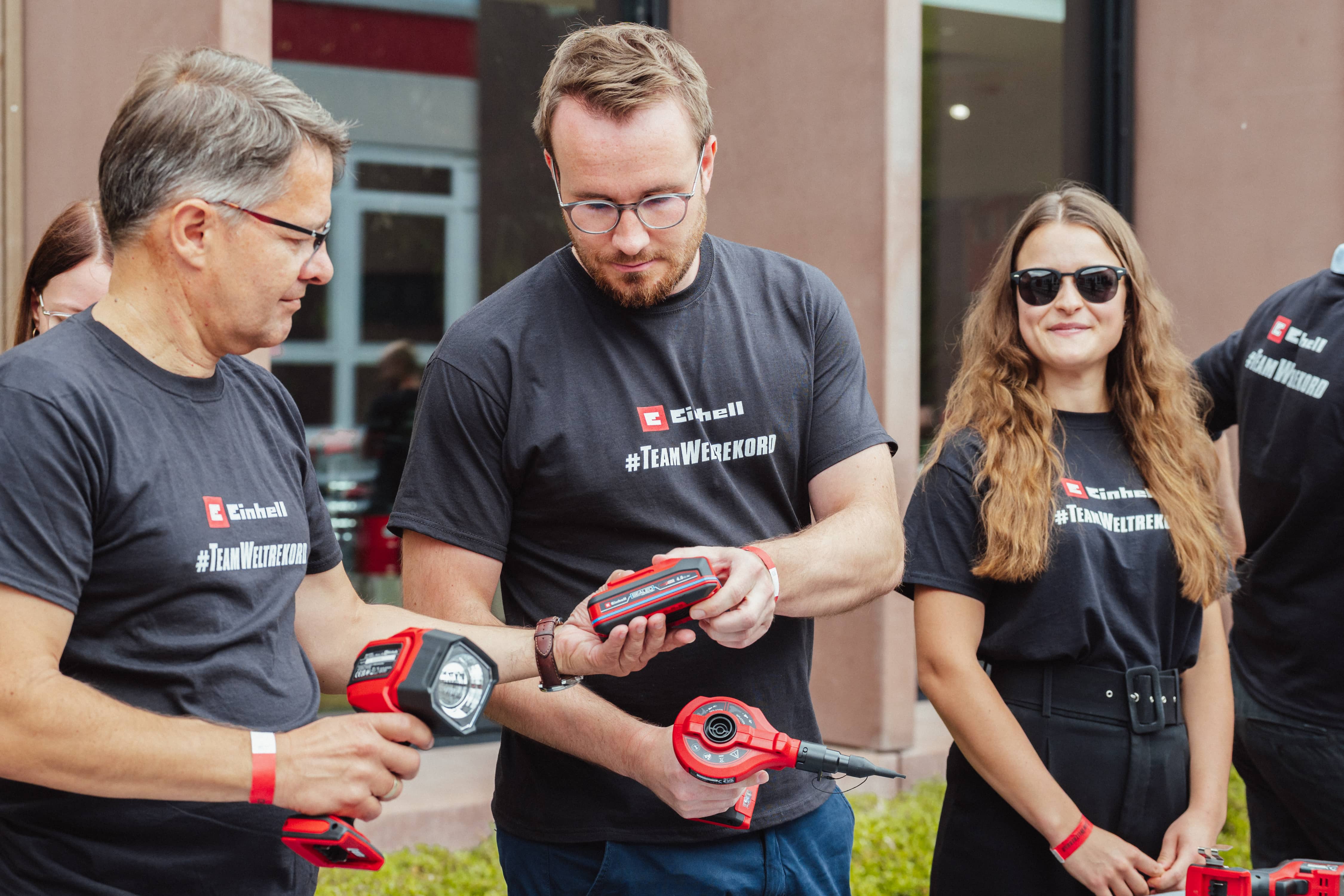 Drei Personen in "#TeamWeltrekord"-Shirts begutachten gemeinsam einen Einhell SEALED Akku.