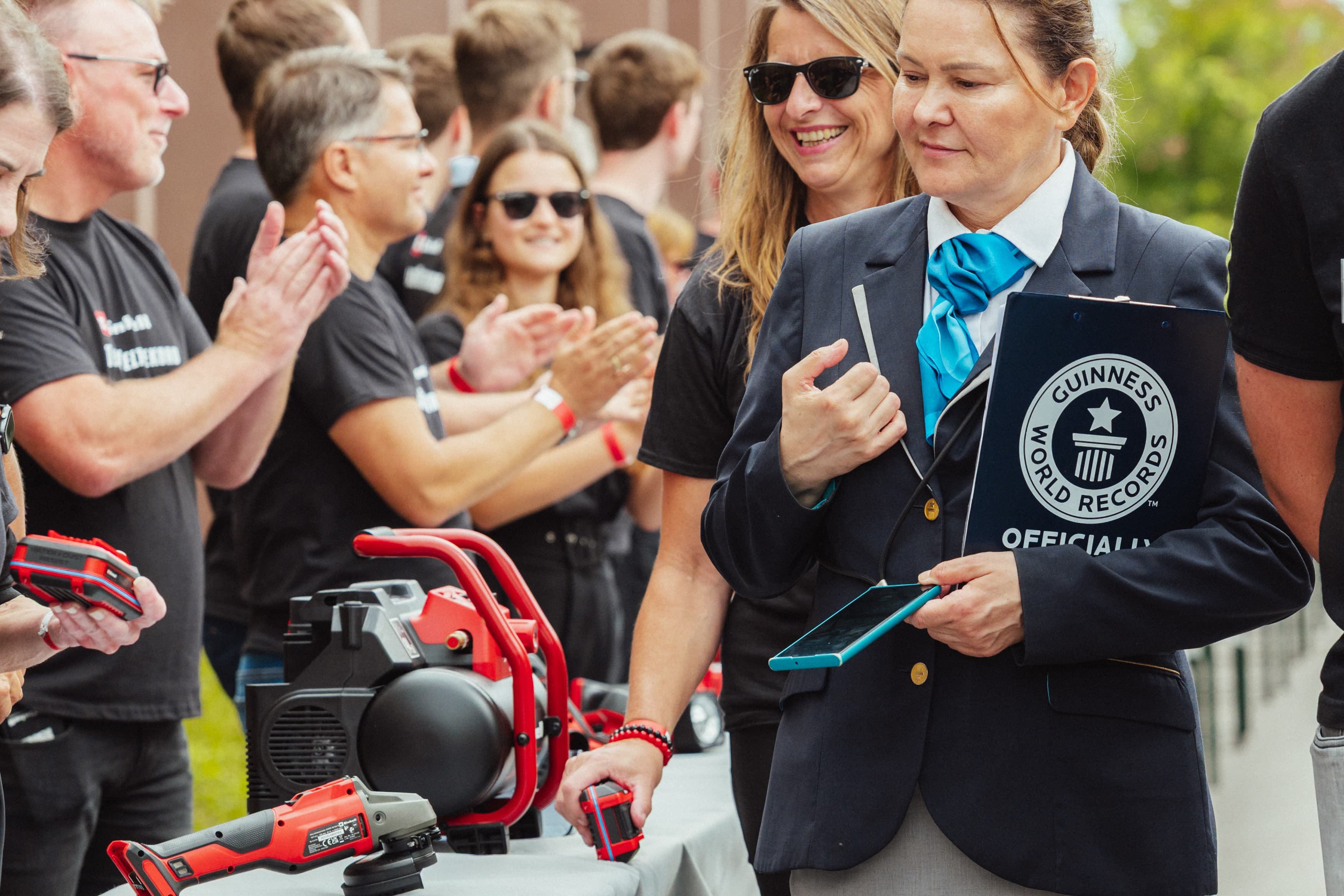 Eine Guinness-Repräsentantin mit Klemmbrett steht neben applaudierenden Personen vor einem Tisch mit Einhell-Geräten.