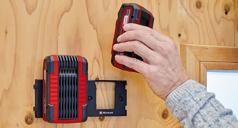 die Einhell Akku-Wandhalterung mit einem Akku und jemand setzt einen weiteren Akku ein