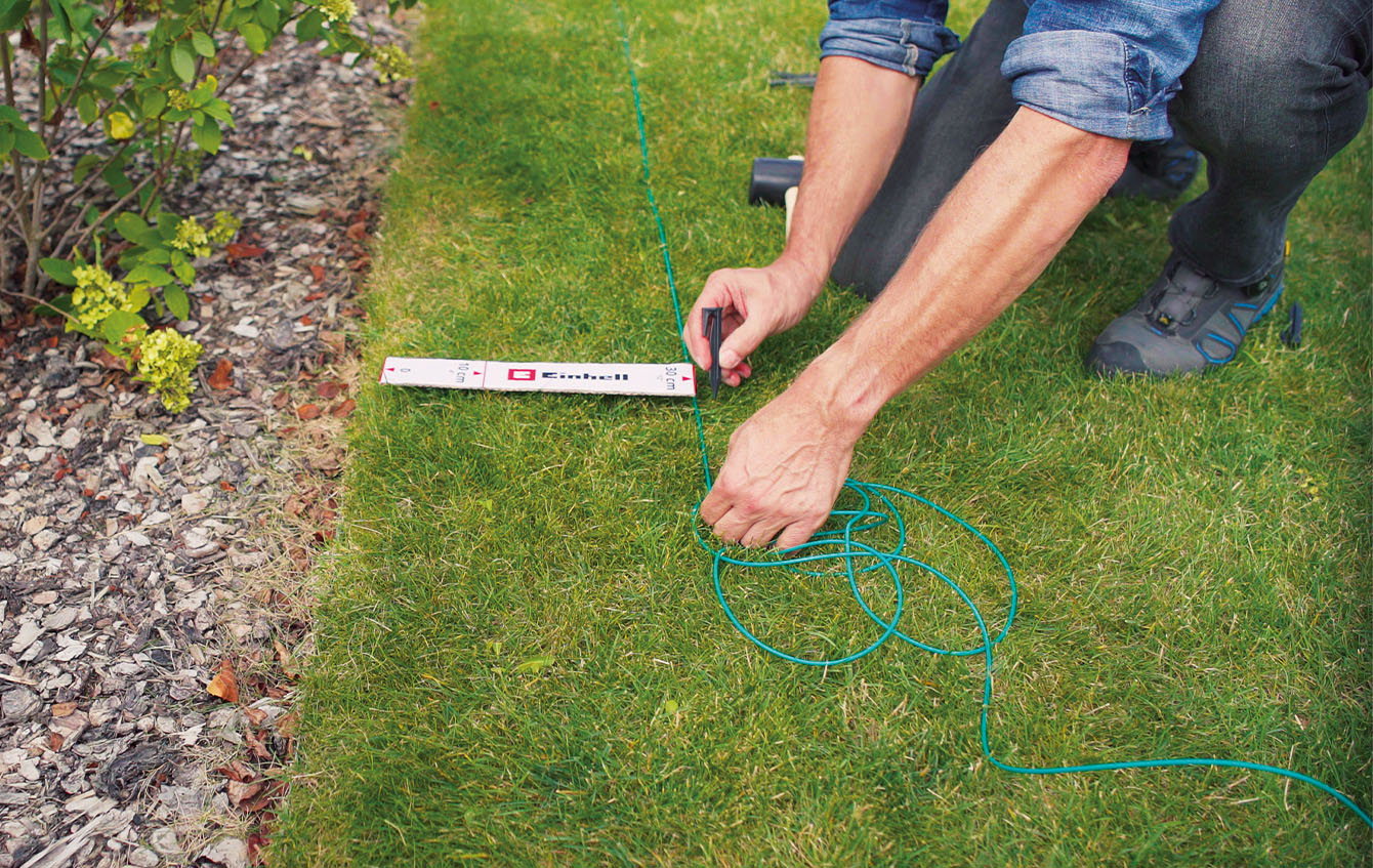 jemand installiert einen Begrenzungsdraht für den Einhell Mähroboter