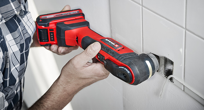 A person uses a Einhell multi-tool to scrape away old silicone.