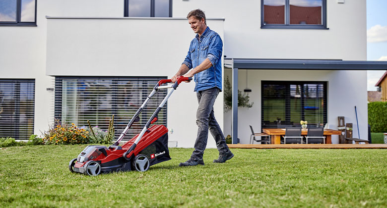 Ein Mann mäht das grüne Gras in seinem Garten mit einem Akku-Rasenmäher.