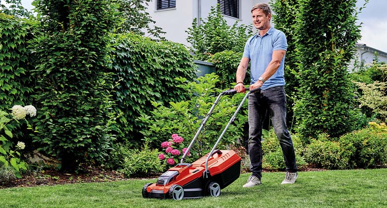 Ein Mann in seinem Garten beim Rasenmähen mit einem Akku-Rasenmäher.