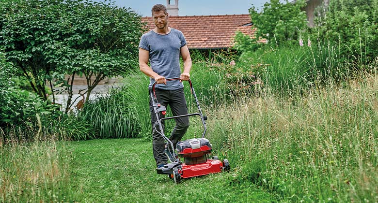 Ein Mann mäht hohes Gras mit einem Akku-Mulchmäher.