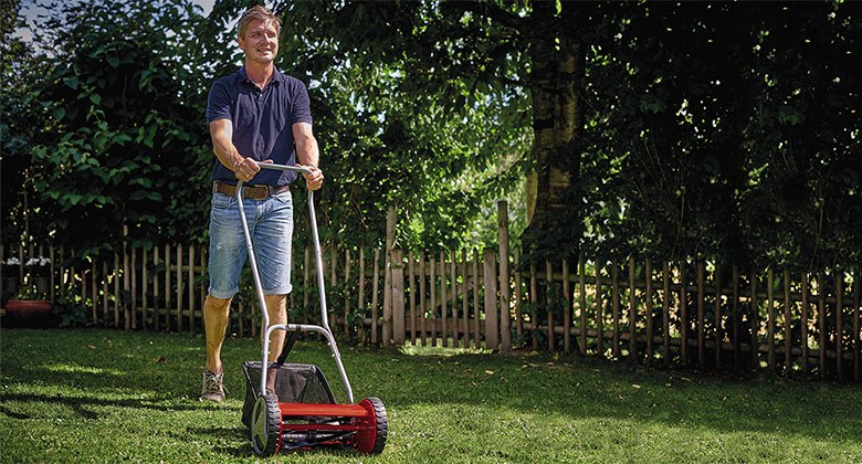 Ein Mann mäht kurzes Gras im Garten mit einem Hand-Rasenmäher.