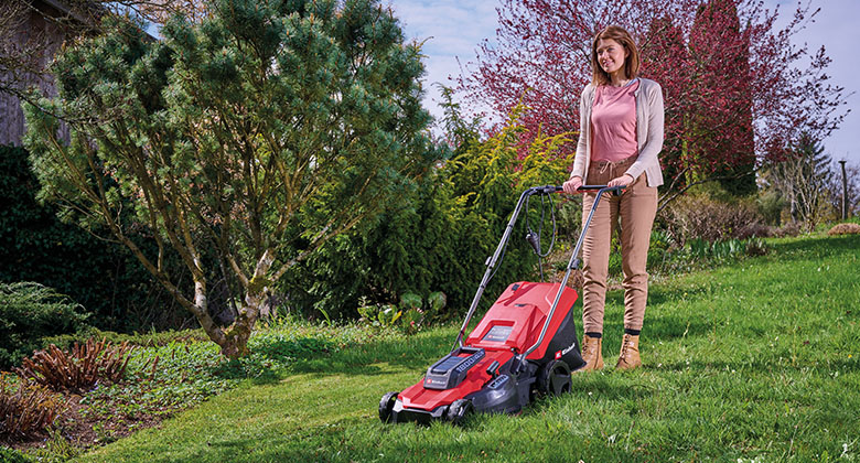 Eine Frau mäht den Rasen in ihrem Garten mit einem Elektro-Rasenmäher.