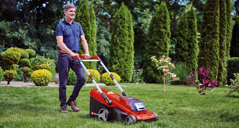 Ein Mann mäht den Rasen in seinem Garten mit einem rot-schwarzen Akku-Rasenmäher.