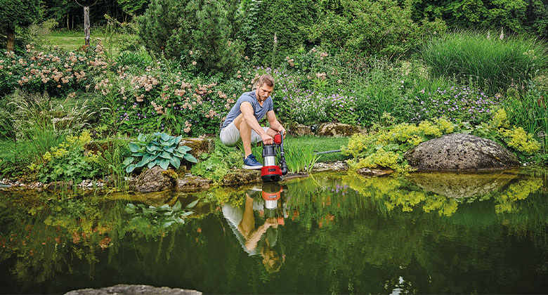 Ein Mann beim Ablassen einer Schmutzwasserpumpe in einen großen Teich, um diesen auszupumpen.