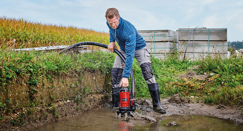 Ein Mann beim Auspumpen einer großen, schmutzigen Wasserpfütze mit Hilfe einer Schmutzwasserpumpe.